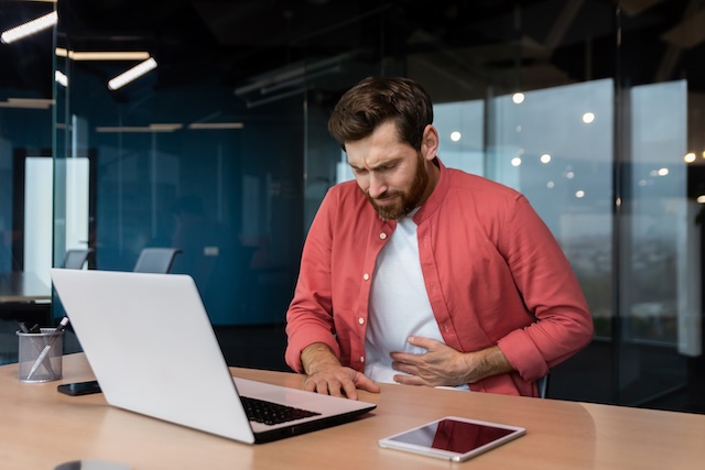 A man in the office at the workplace is sick, he has a severe stomach ache, the businessman got food poisoning from lunch, he is sitting at the table inside the building