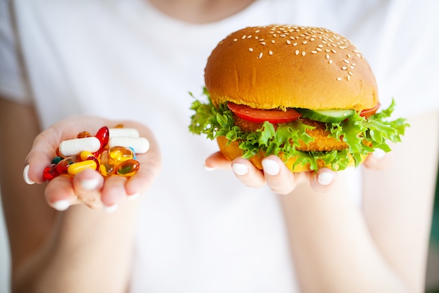 A woman holds pills and a harmful burger in her hands