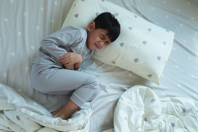 Top View of Asian boy lying in bed with stomach ache